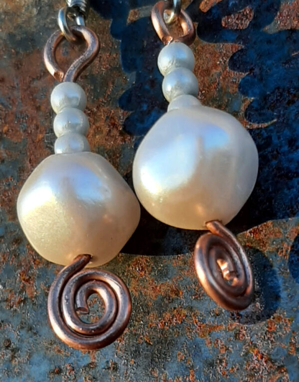 Each earring has a round white bead below three round pale blue beads. All are strung on copper wire that ends at the bottom in a neat spiral.