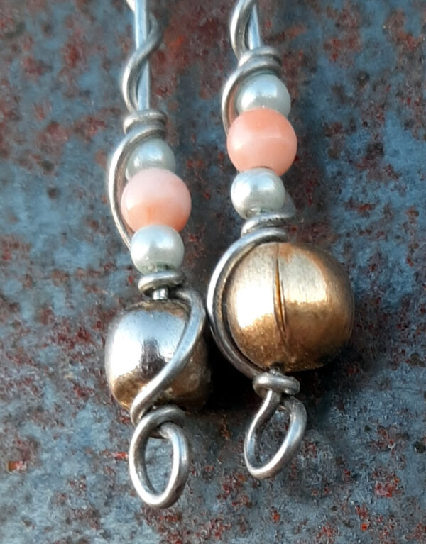 Each earring has a round brass bead at the bottom, with two smaller pale blue beads surrounding a peach bead above it, all strung on steel wire that curves back up around each bead, then twists around itself.