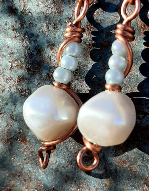 Copper wire earrings, hinged at the middle; at the top, copper wire wrapping around itself; below, a single white bead with three tiny pale blue beads above.