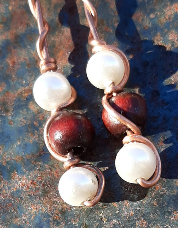 Each earring has a round red wooden bead with white beads above and below, all strung on copper wire that curves back up around each bead, then twists around itself.