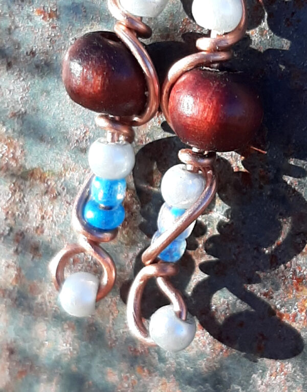 Each earring has a round red wooden bead with white and tiny blue beads above and below, all strung on copper wire that curves back up around each bead, then twists around itself.