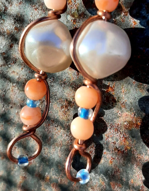 Each earring has a round white bead with peach and tiny blue beads above and below, all strung on copper wire that curves back up around each bead, then twists around itself.