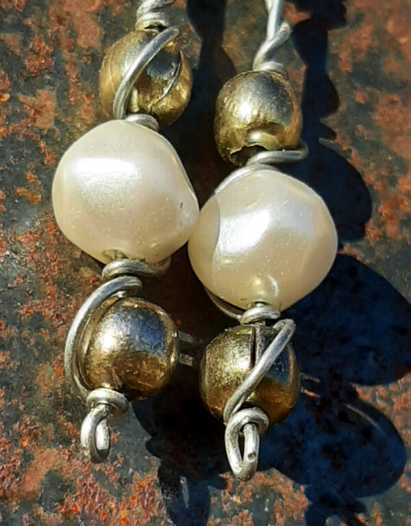 Each earring has two round brass beads to either side of a larger white bead, all strung on steel wire that curves back up around each bead, then twists around itself.