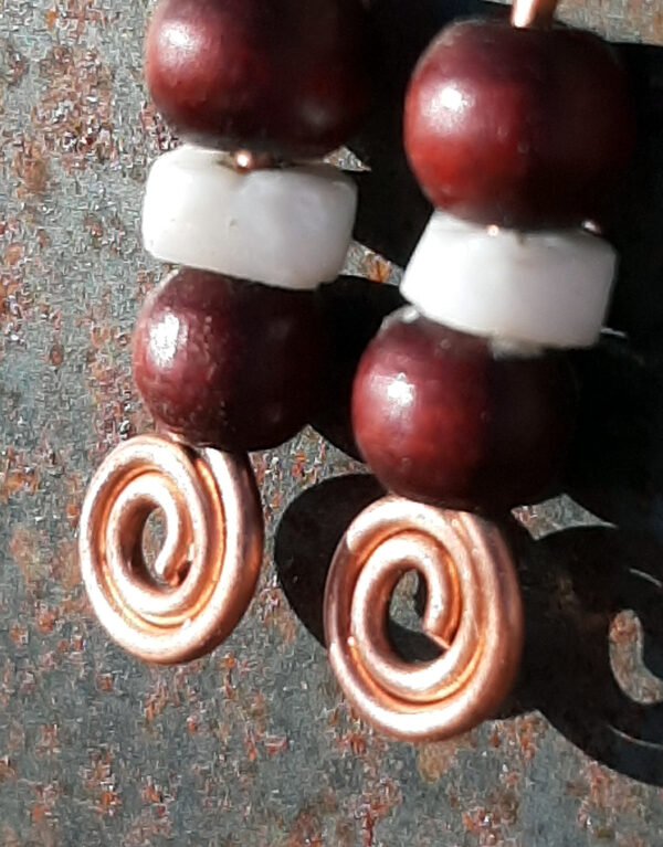 Each earring has two round red wooden beads with a disc-shaped bone bead in between. All are strung on copper wire that ends at the bottom in a neat spiral.