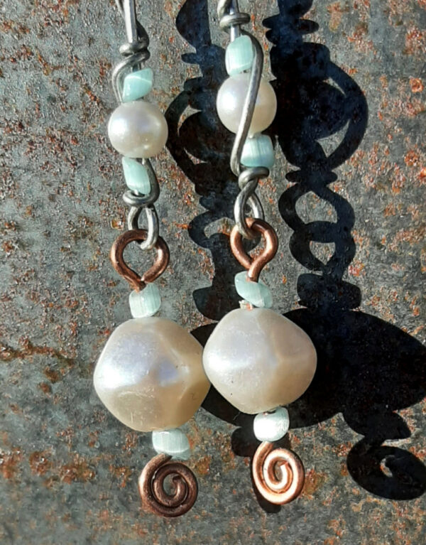 Each earring has two sections. The lower has a large white bead with a smaller pale blue bead above and below, all strung on copper wire with a neat spiral at the bottom. This is linked to a piece with pale blue beads above and below a white bead that's scarcely larger, all strung on steel wire that curves back up around each bead, then twists around itself.