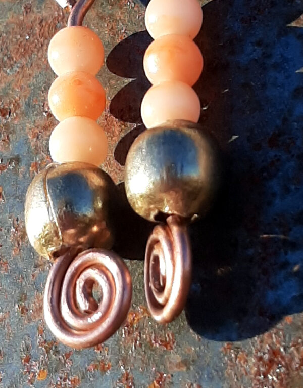 Each earring has a round brass bead below three round peach-colored beads. All are strung on copper wire that ends at the bottom in a neat spiral.