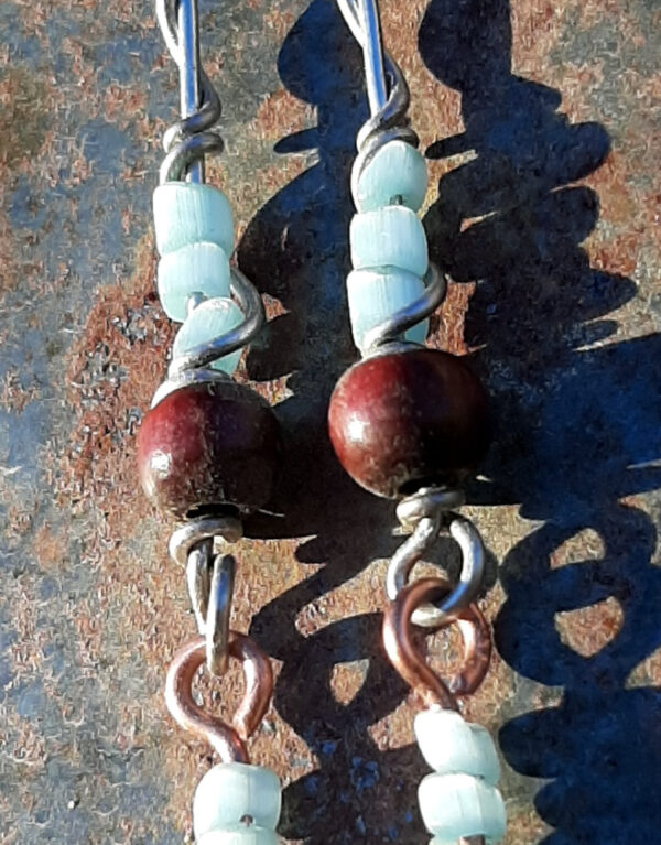 Each earring has two sections. The lower has three pale blue beads strung on copper wire with a neat spiral at the bottom. This is linked to a piece with pale blue beads above a round red wooden bead, all strung on steel wire that curves back up around each bead, then twists around itself.