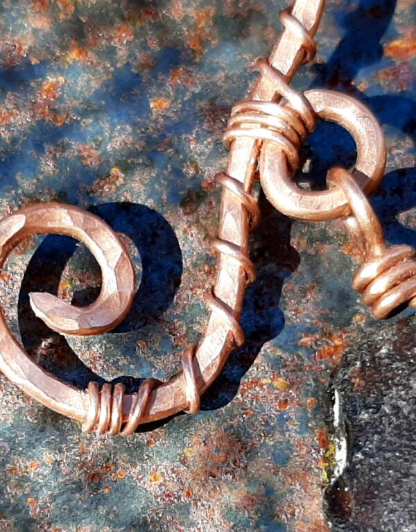 A coke-bottle brown piece of creek glass, wrapped in copper wire, hangs from a curled and curved piece of much thicker hammered copper wire.