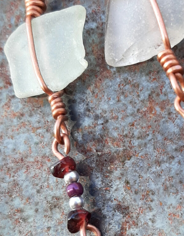 Each earring has a roughly rectangular piece of white creek glass, simply wrapped in copper wire, from which hangs another short length of copper with purple and silver-colored beads threaded onto it.