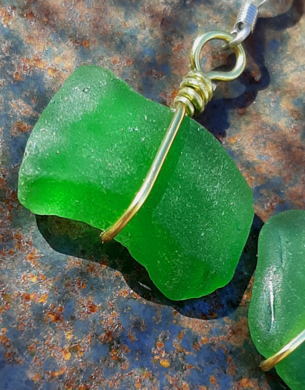 Each earring is a very roughly rectangular piece of green creek glass, simply wrapped in a single loop from top to bottom with gold-colored wire.