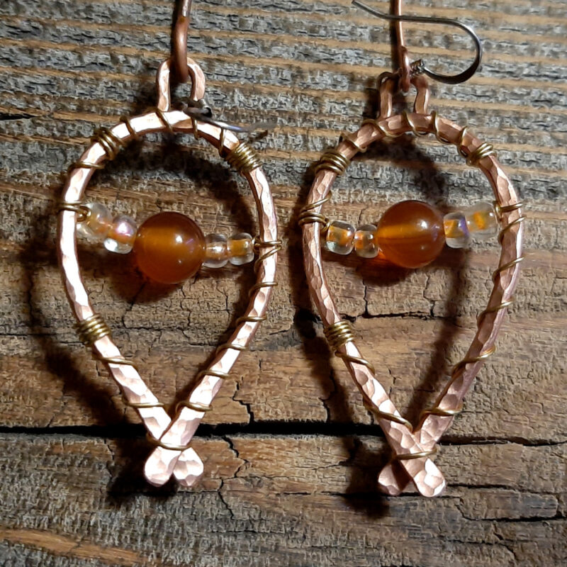 Each earring is hammered copper wire bent into a horseshoe shape, with brownish-orange beads draped across.