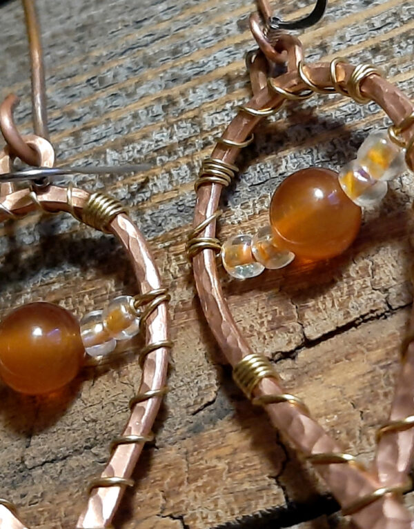 Each earring is hammered copper wire bent into a horseshoe shape, with brownish-orange beads draped across.