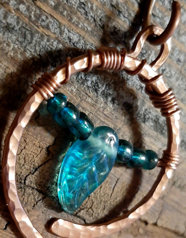 A hammered copper circle, almost, the ends not quite meeting at the bottom. Festooned across are teal green glass beads, a leaf between matching seed beads.