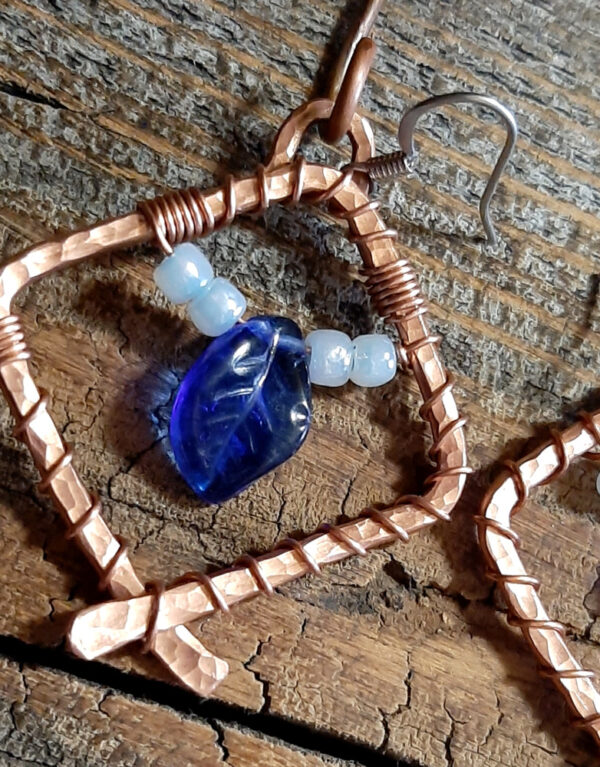 Each earring is a diamond shape of hammered copper wire, glass beads festooned within -- a cobalt blue leaf between white seed beads.