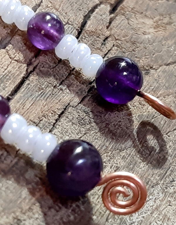 Each earring is an s-shaped piece of hammered copper wire, with strung white and purple beads dangling below.