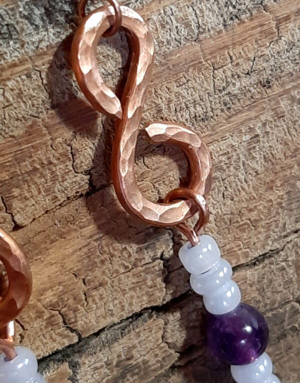 Each earring is an s-shaped piece of hammered copper wire, with strung white and purple beads dangling below.