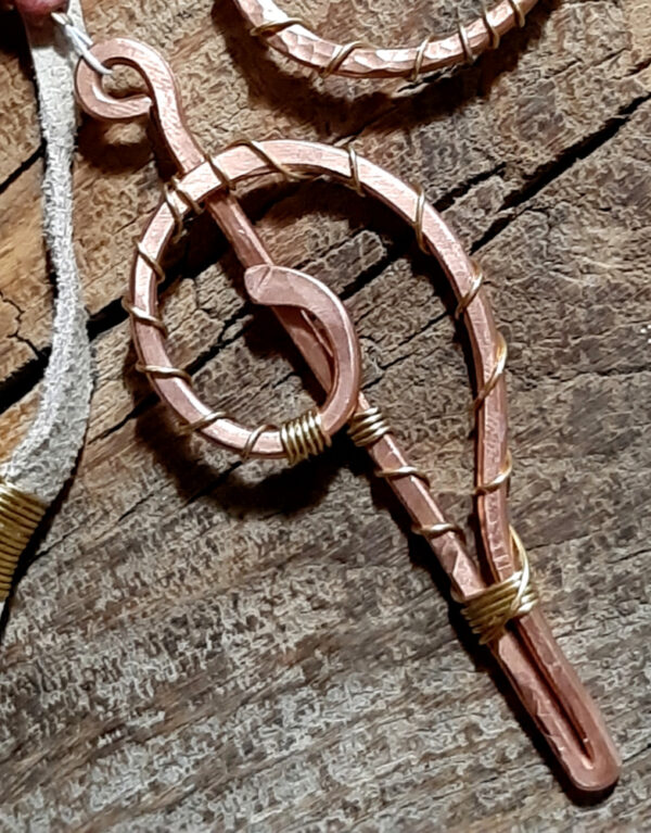 This pendulum starts at the top with a loop of hammered copper, and ends with more copper that crops straight down and then curves back up into a spiral. In between are a length of off-white leather thing, and grey-brown jasper strung with smaller brown beads.