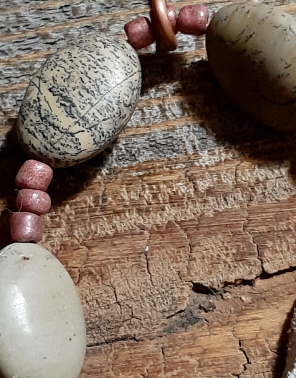 This pendulum starts at the top with a loop of hammered copper, and ends with more copper that crops straight down and then curves back up into a spiral. In between are a length of off-white leather thing, and grey-brown jasper strung with smaller brown beads.