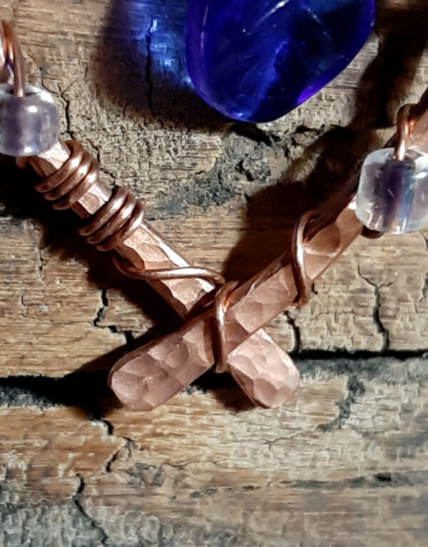 Each earring is hammered copper wire bent into a horseshoe shape, with clear glass beads wired onto it at intervals; in the center hang cobalt blue glass leaves.