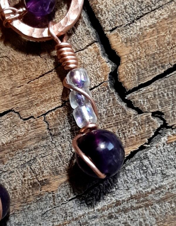 Each earring is hammered copper in a rough s shape, with amethyst and clear glass beads hanging below.