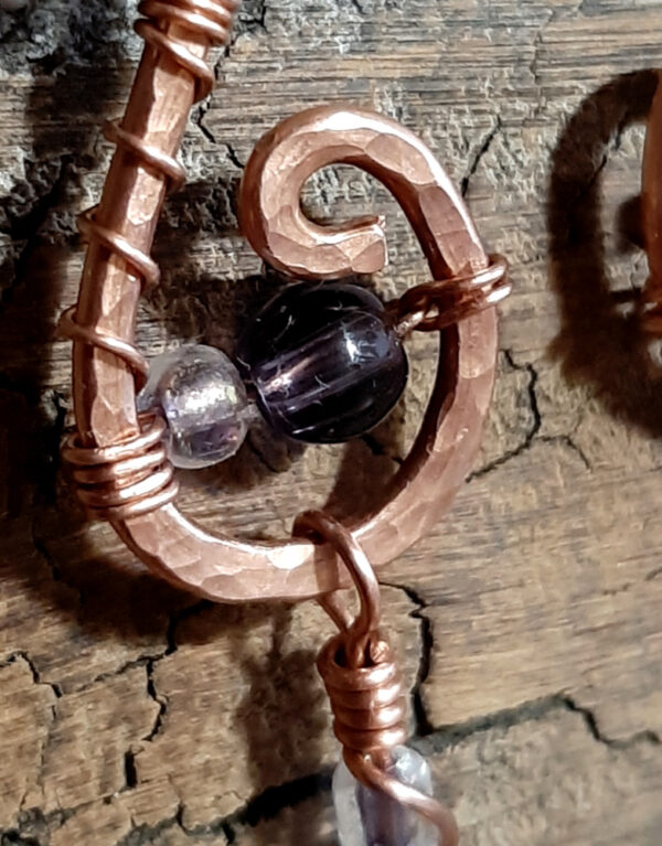 Each earring is hammered copper in a rough s shape, with amethyst and clear glass beads hanging below.