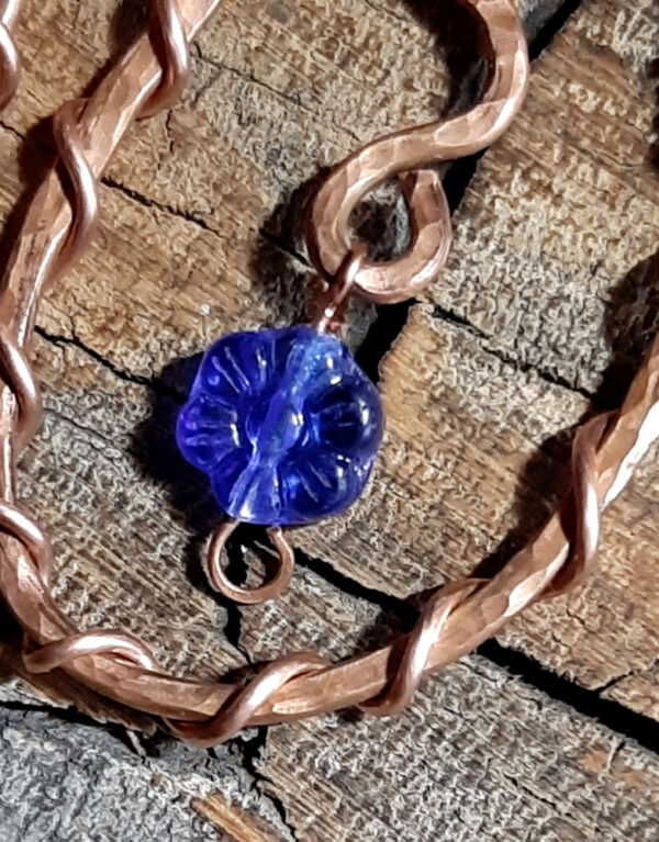 Each earring is an oval of hammered copper wire, with a flower-shaped cobalt blue glass bead suspended within.