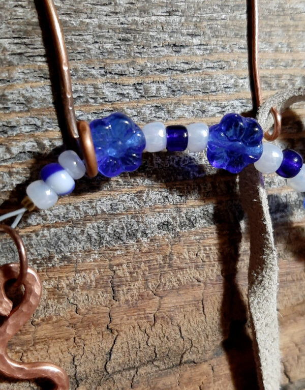 This pendulum features a squiggly pointer on one end and an oval finger loop on the other, both of hammered copper wire, with strung blue and white beads and a length of off-white leather thong in between.