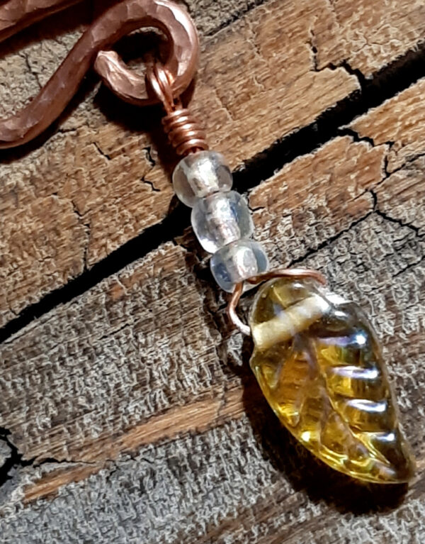 A squiggle of hammered copper wire; three small clear beads and a yellow glass leaf hang from the bottom.