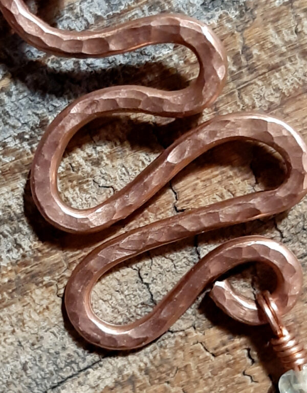 A squiggle of hammered copper wire; three small clear beads and a yellow glass leaf hang from the bottom.