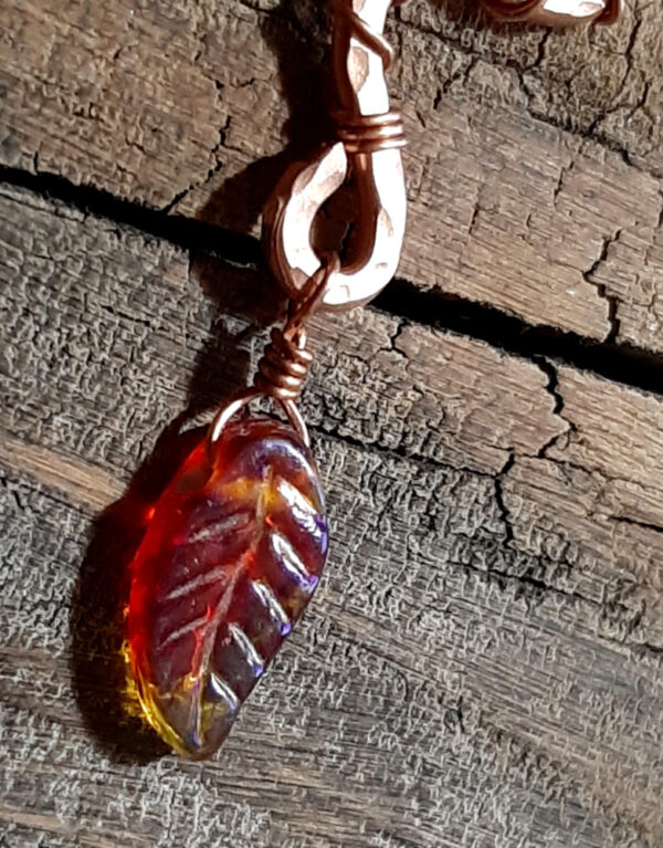 A squiggle of hammered copper wire; a rusty red glass leaf hangs from the bottom.