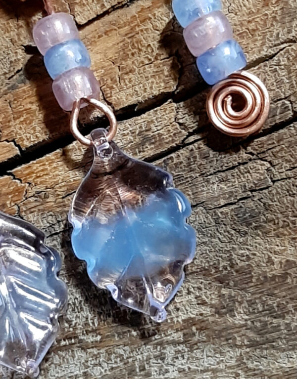 Each earring is an uneven arch of hammered copper, with three pink and pale blue beads hanging from the short end, and three pink and pale blue beads with a big clear, pink, and blue leaf hanging from the other.