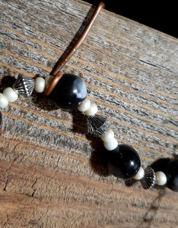 The pendulum has a silver-colored ring set with a black eye-shaped stone on one end. The pointer on the other end is gold-colored, with black, white, & grey beads in between.