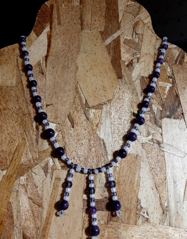 This necklace has alternating white and purple beads, with three short lengths of the same beads dangling from the center front.