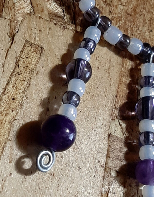 This necklace has alternating white and purple beads, with three short lengths of the same beads dangling from the center front.