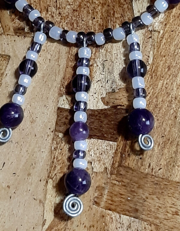 This necklace has alternating white and purple beads, with three short lengths of the same beads dangling from the center front.